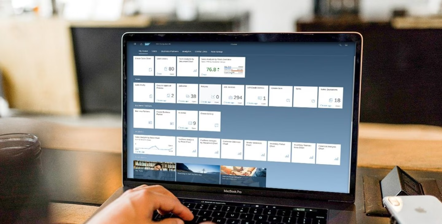 Interface SAP Business One affichée sur un MacBook Pro avec tableaux de bord et indicateurs de performance en environnement de travail.