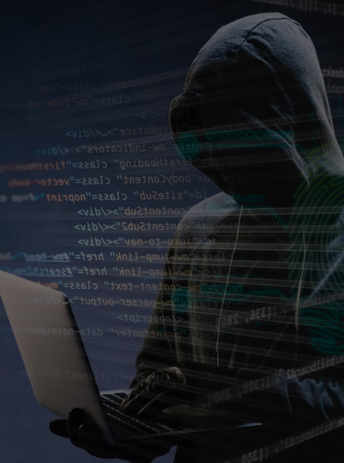 Personne encapuchonnée tapant sur un ordinateur portable, représentant une cyberattaque ou une activité malveillante sur fond de code