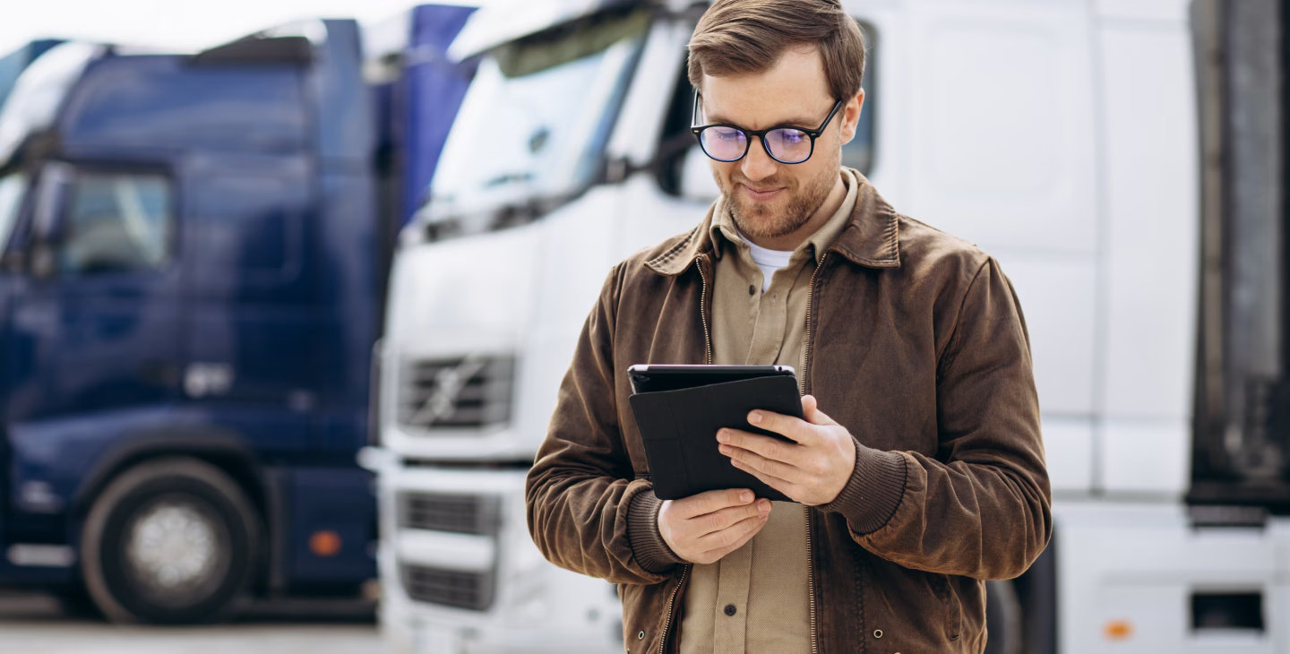 Responsable logistique utilisant une tablette pour gérer une interface transporteur SAP Business One devant des camions.