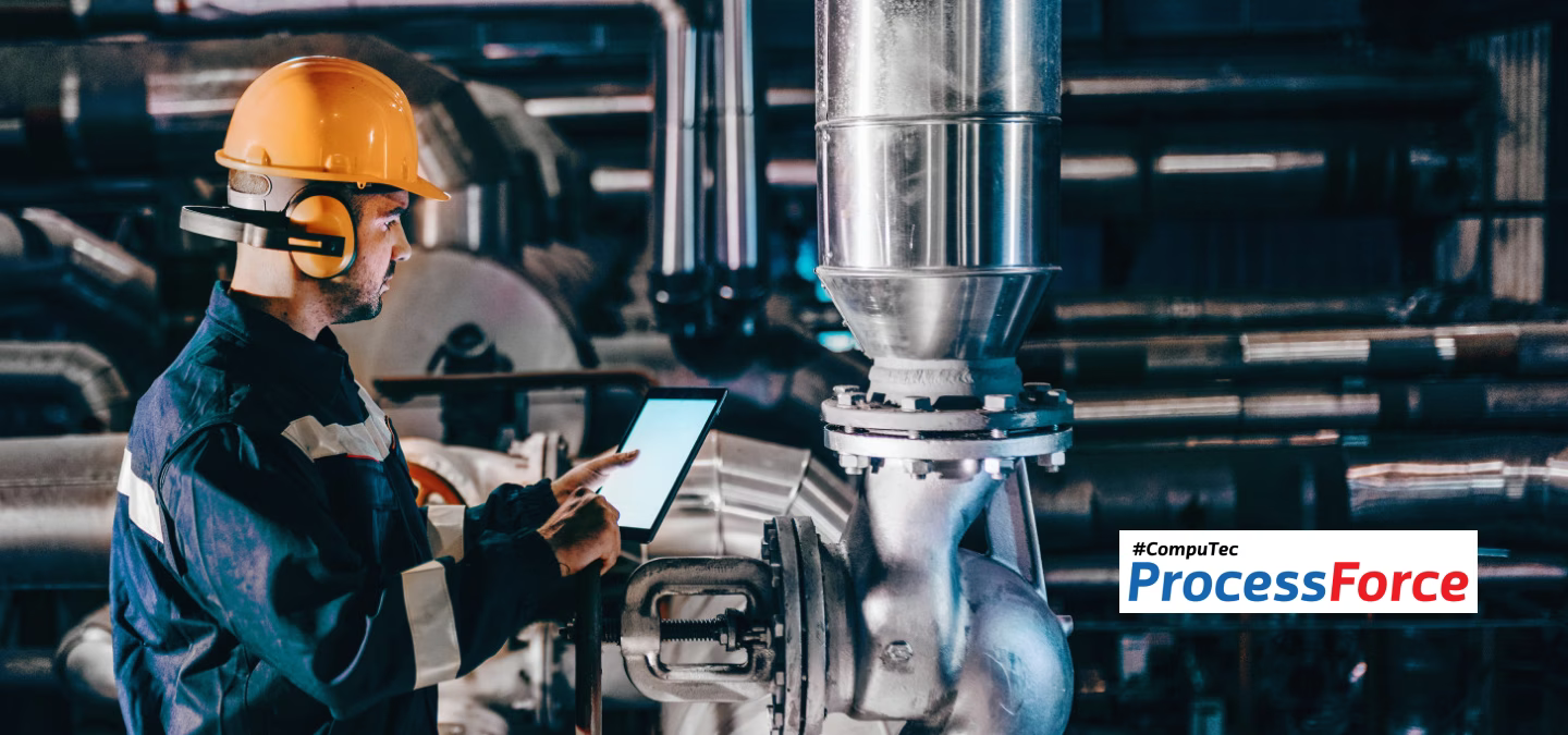 Un opérateur industriel en casque et protection auditive contrôle une installation de production à l’aide d’une tablette.