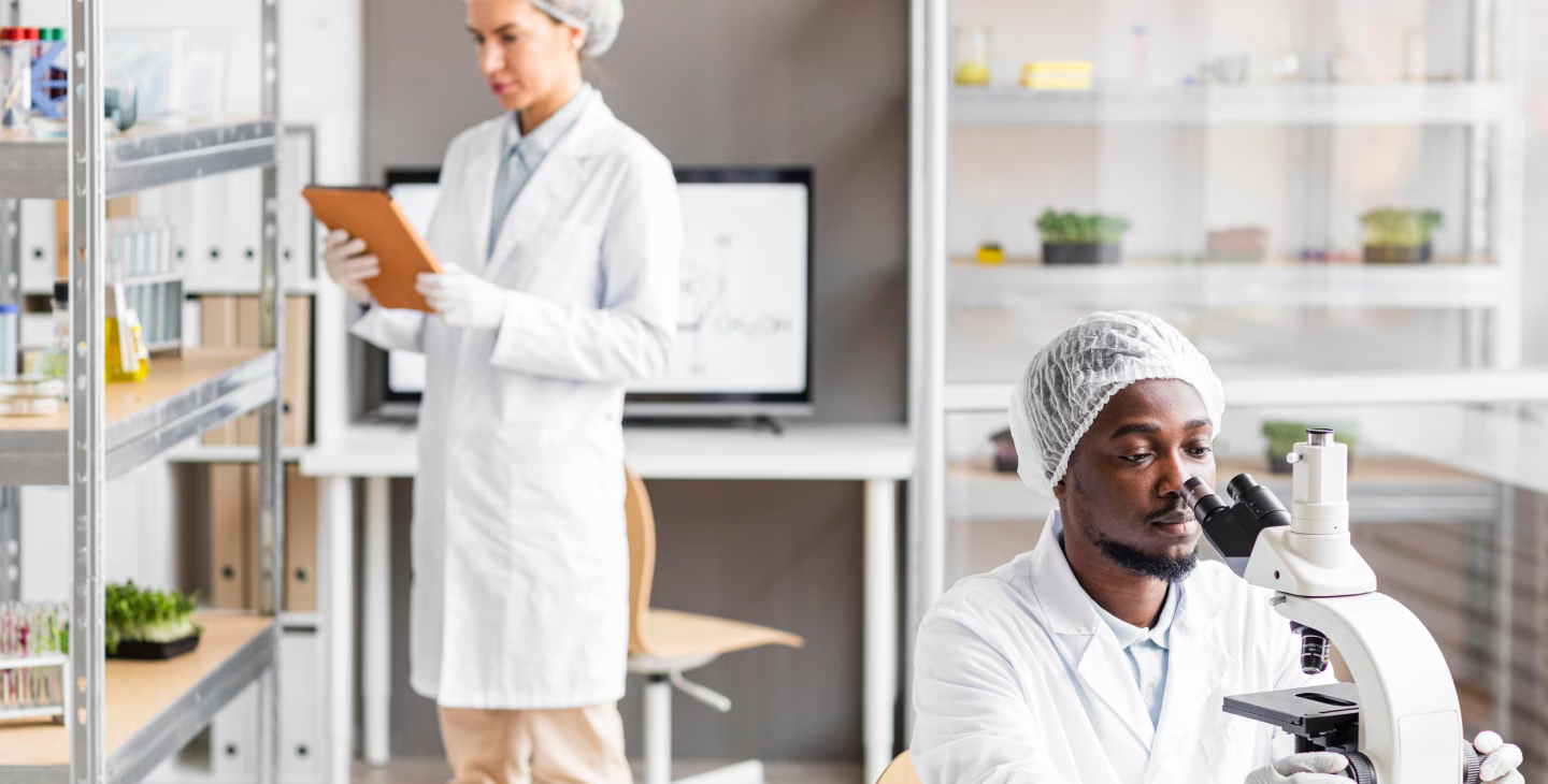 Techniciens en laboratoire effectuant des contrôles qualité à l’aide d’un microscope et d’une tablette numérique.